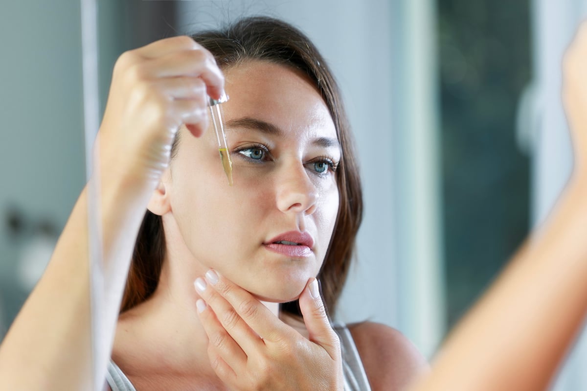 Young woman dropping hyaluronic acid from pipette on face. Concept of face skin care