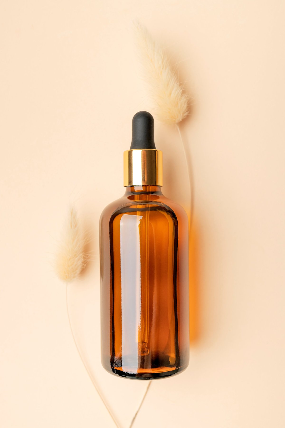 Cosmetics mockup. Amber-brown glass bottles with dropper pipette and spikelets of dried flowers on beige background. Beauty and face care concept, serum, oil. Natural cosmetics packaging design